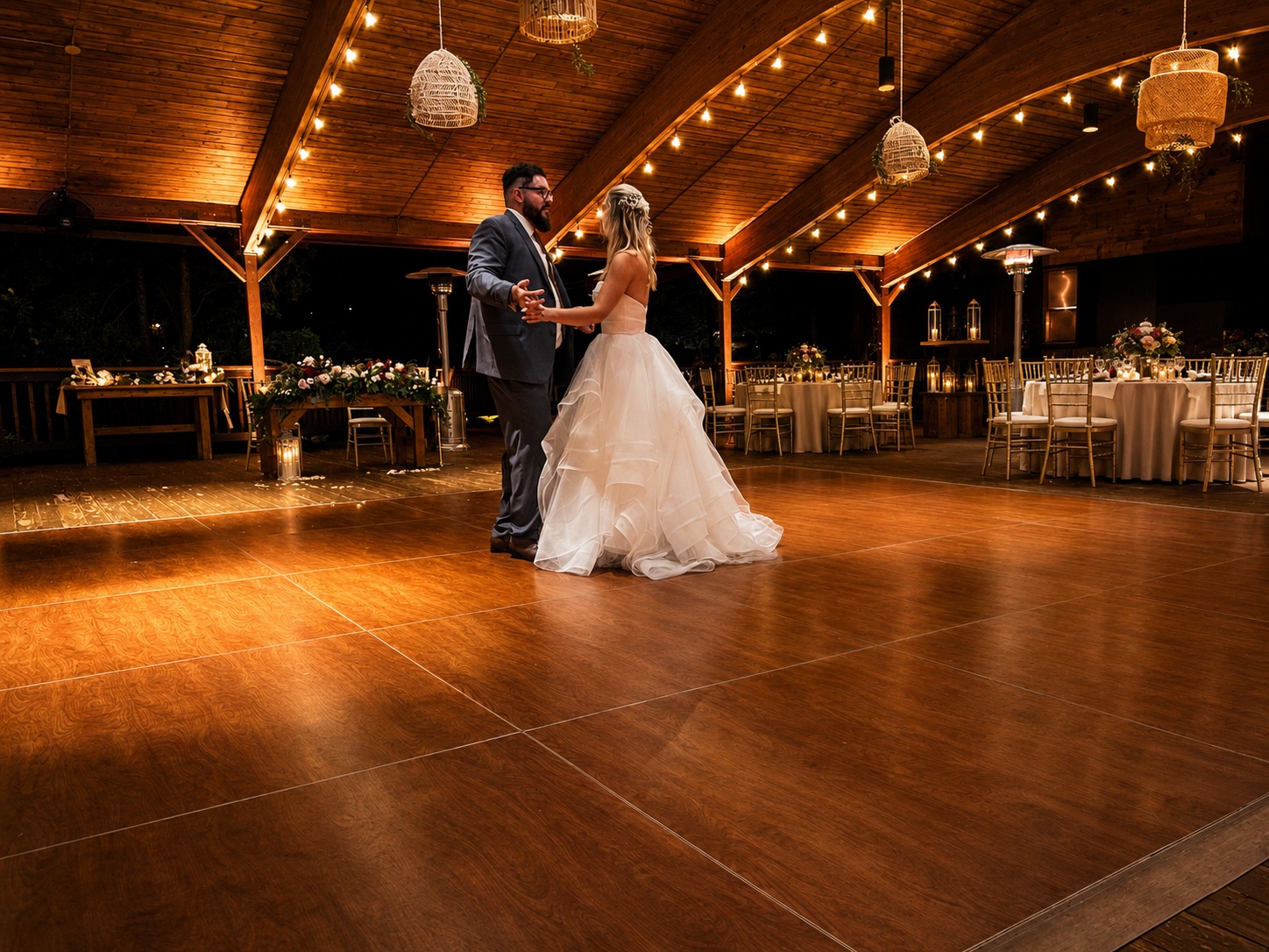 Bride and groom share a first dance on a wood dance floor under warm string lights and amber uplighting at Minerals Hotel & Spa
