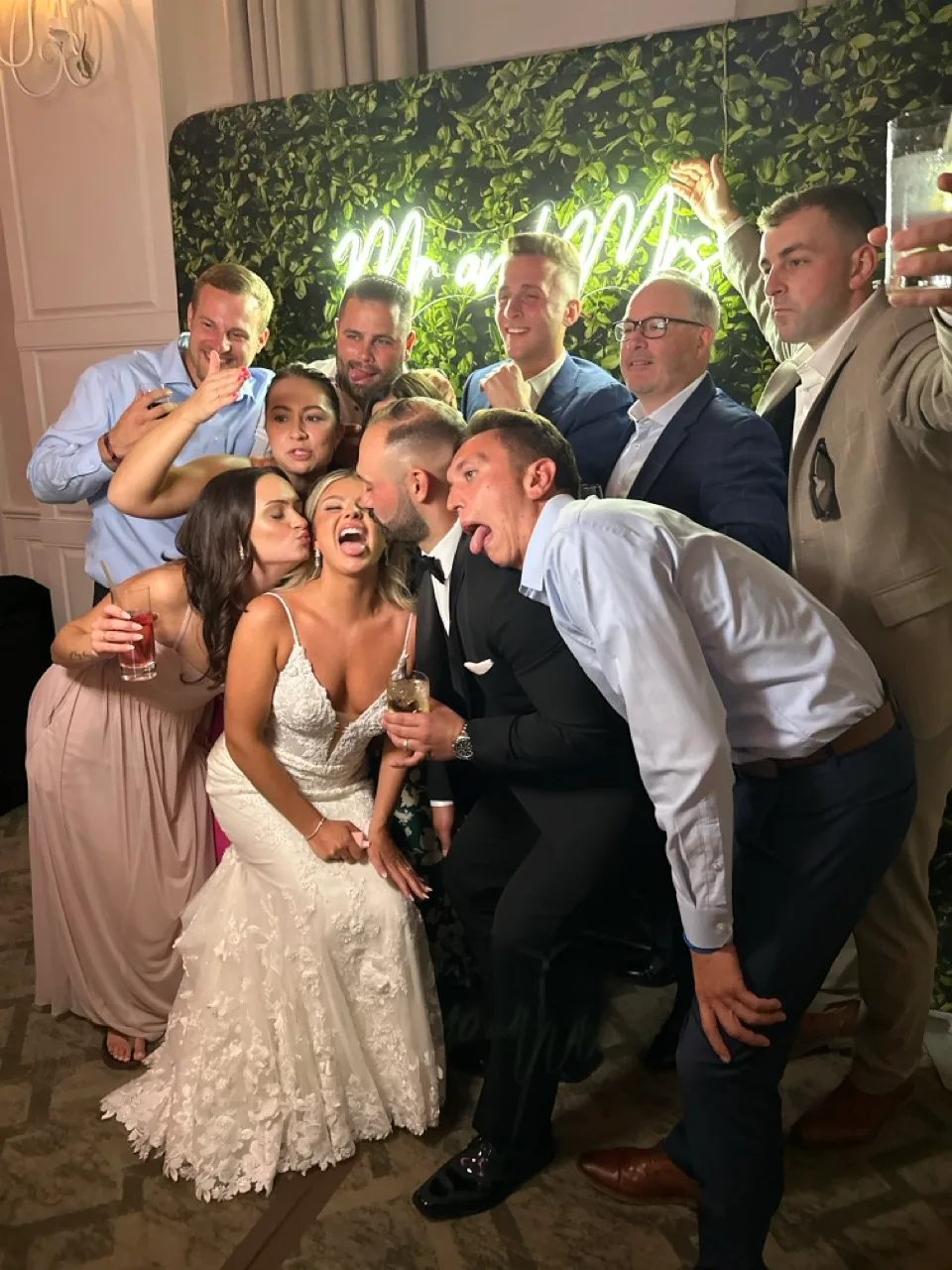 Newlyweds and guests posing together at the greenery photo booth backdrop
