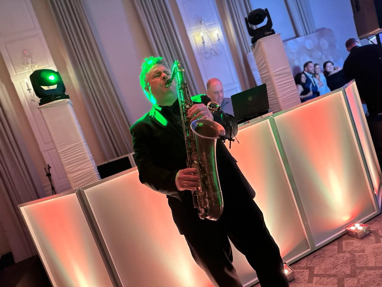 Saxophonist performing beside an illuminated DJ booth during a Grand Cascades reception