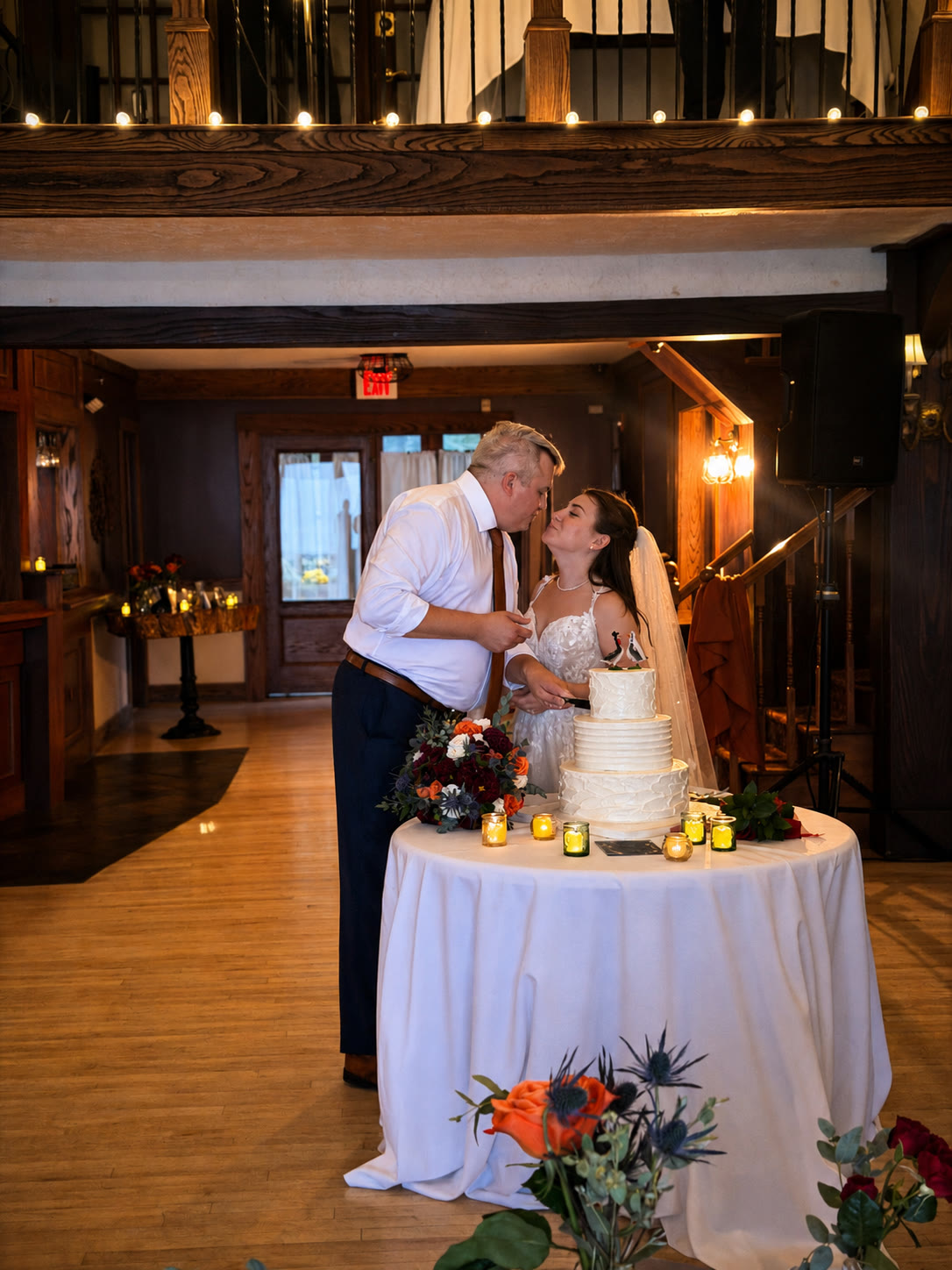 Newlyweds cutting their wedding cake in the timber-beamed reception room at Lake Valhalla Club, lit by warm candlelight and string lights