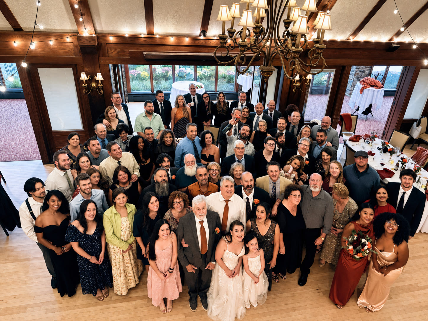 Full wedding party and guests gathered for a group photo beneath the chandelier in the Lake Valhalla Club ballroom