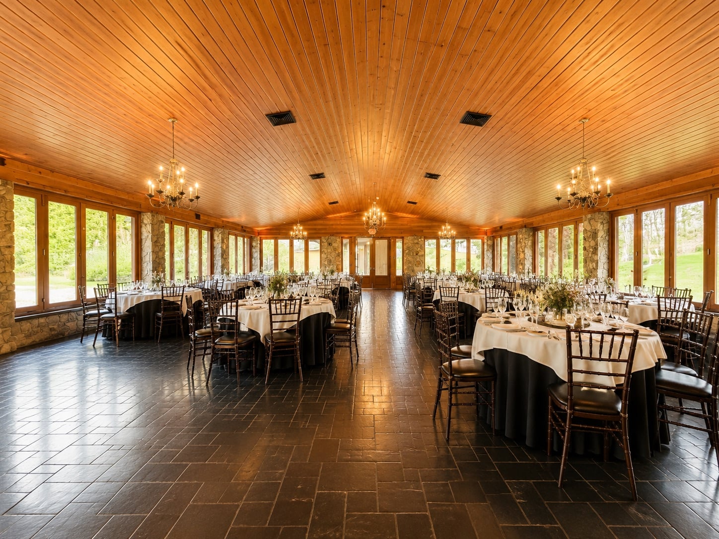 Lawnhaven at Stroudsmoor by Wedgewood Weddings — glass-walled pavilion with stone columns and pitched wood ceiling before uplighting, lit only by chandeliers and daylight