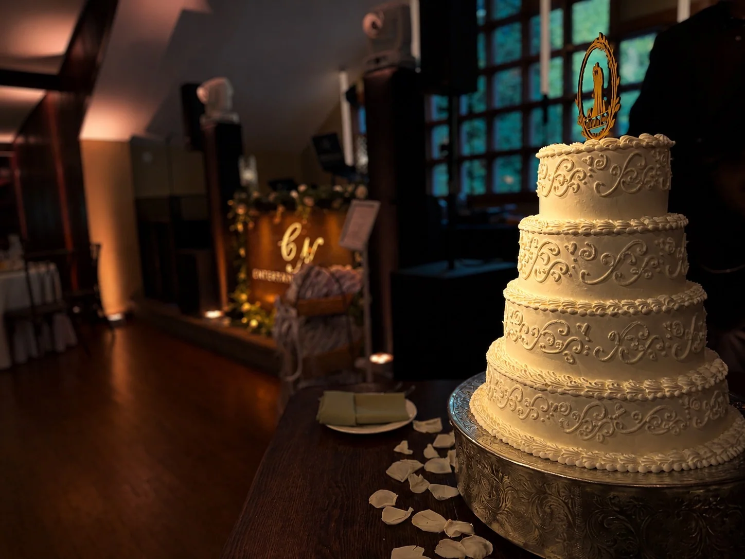 Warm pin spot lighting illuminating the scrollwork on a four-tier wedding cake at Woodsgate at Stroudsmoor by Wedgewood Weddings