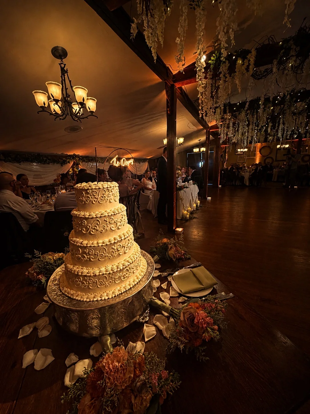 Pin spot lighting highlighting a four-tier wedding cake in the candlelit Woodsgate reception room at Stroudsmoor by Wedgewood Weddings