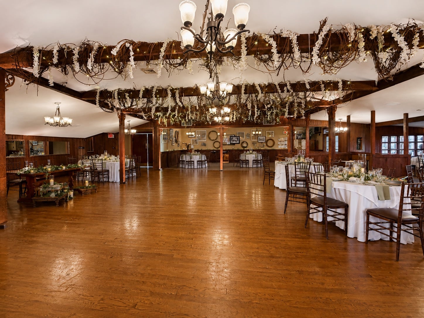 Woodsgate at Stroudsmoor by Wedgewood Weddings — restored stone-and-oak barn before uplighting, lit only by chandeliers and twig-and-floral beam décor